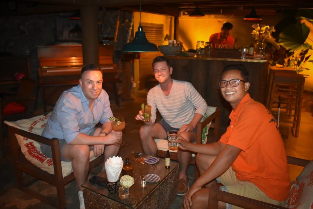 Three guests with drinks in a warmly lit bar at the end of the evening