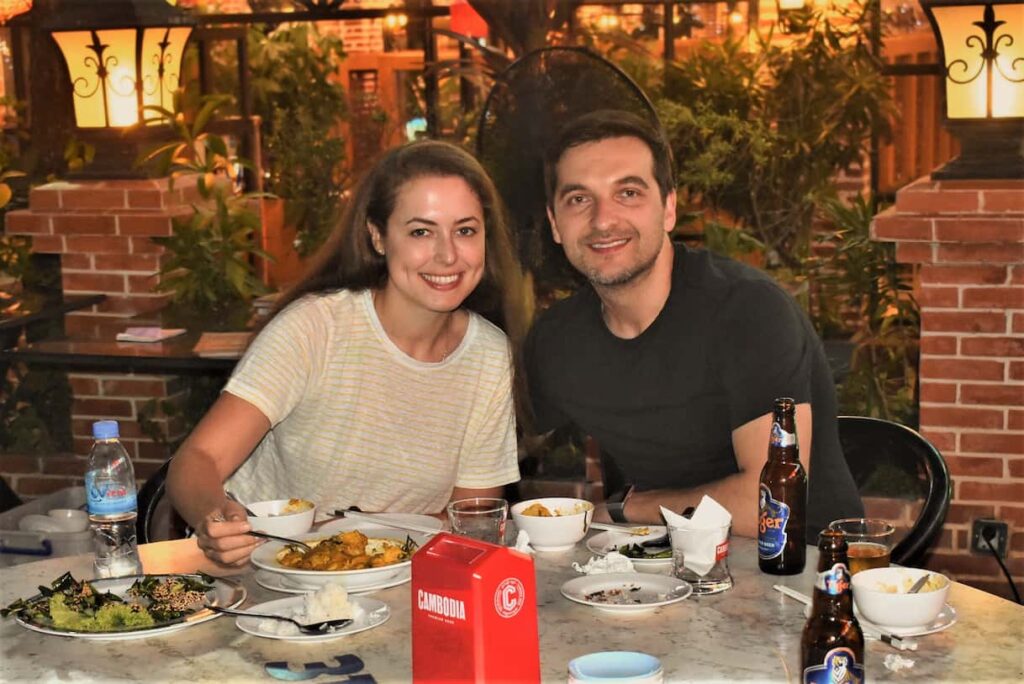 Two guests at a sit-down Khmer dinner with shared dishes and cold beer